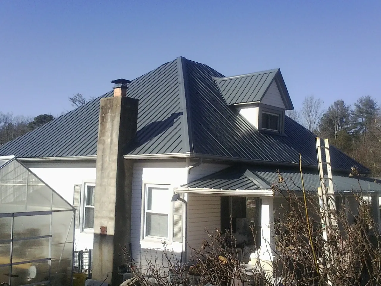 Dark blue standing seam metal roof on a white farmhouse with dormer — Slate & Tile Roof Repair by Roofing Brothers in Bentley