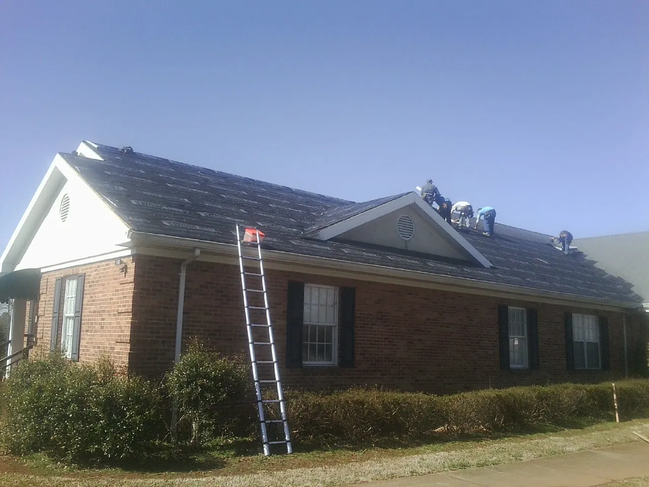 Crew tearing shingles off a brick ranch roof with a ladder set — Emergency Roof Repair work by our crew in Bentley