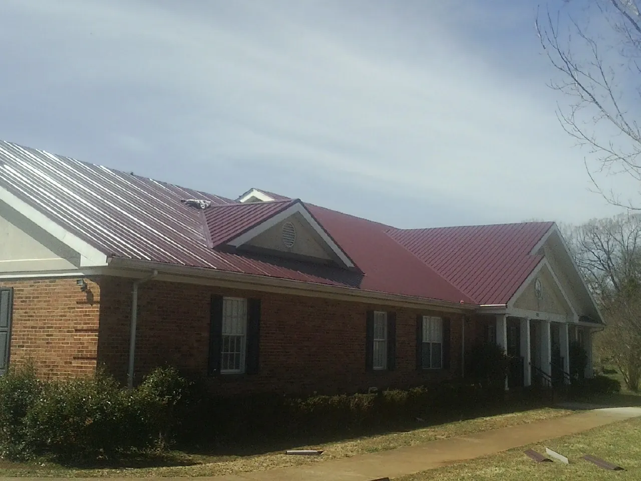 Red metal roof with gabled entries on a long brick building, from a Hail Damage Roof Repair job in Bentley
