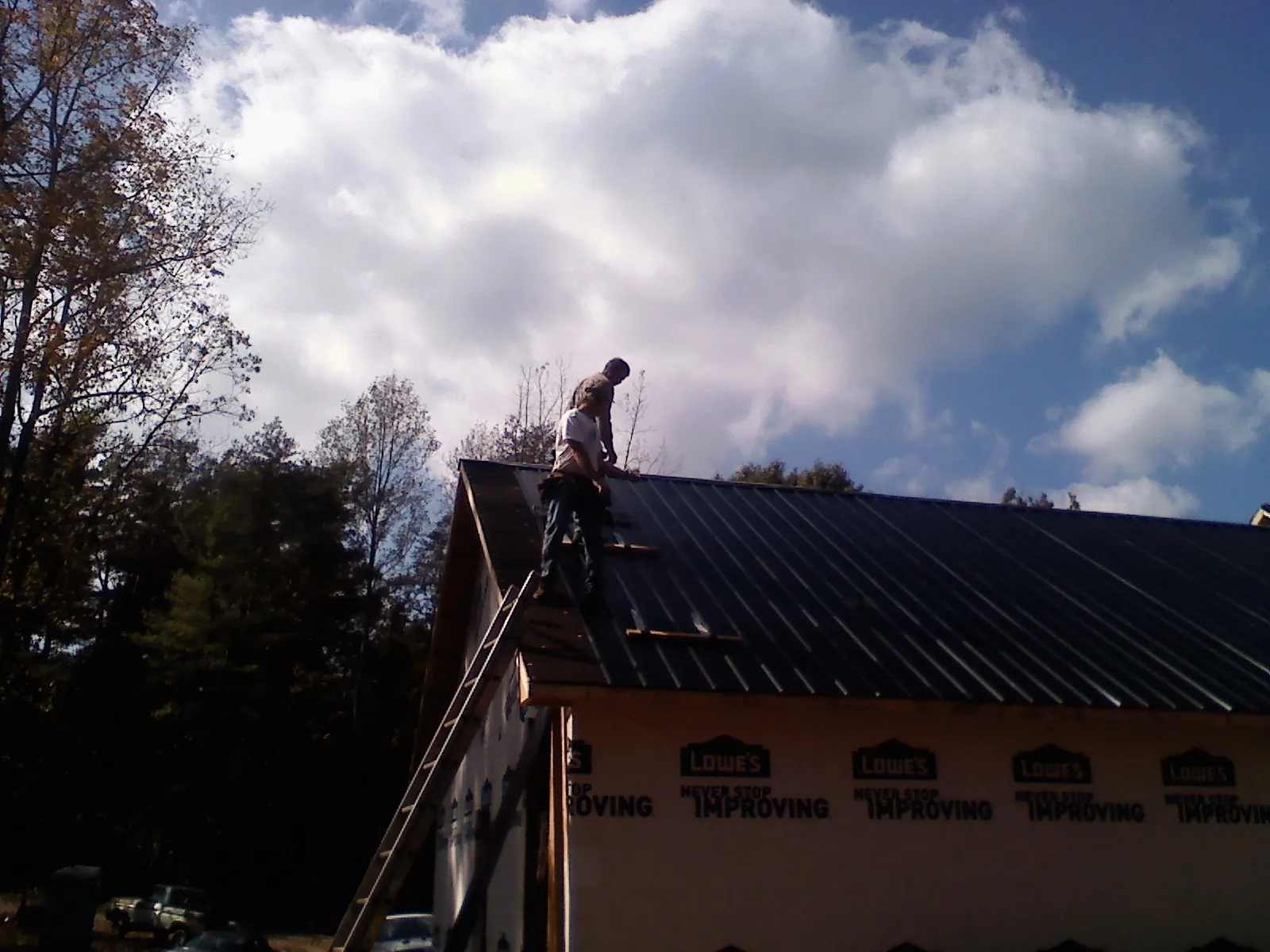 Roofer fastening dark metal panels high against a cloudy sky, from a Roof Inspection job in Bentley