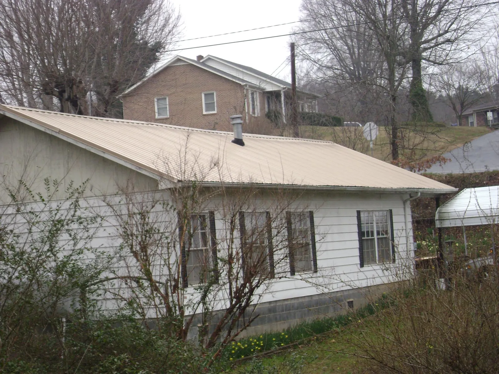 Tan metal roof on a white sided house set into a hillside — Commercial Roofing by Roofing Brothers in Bentley