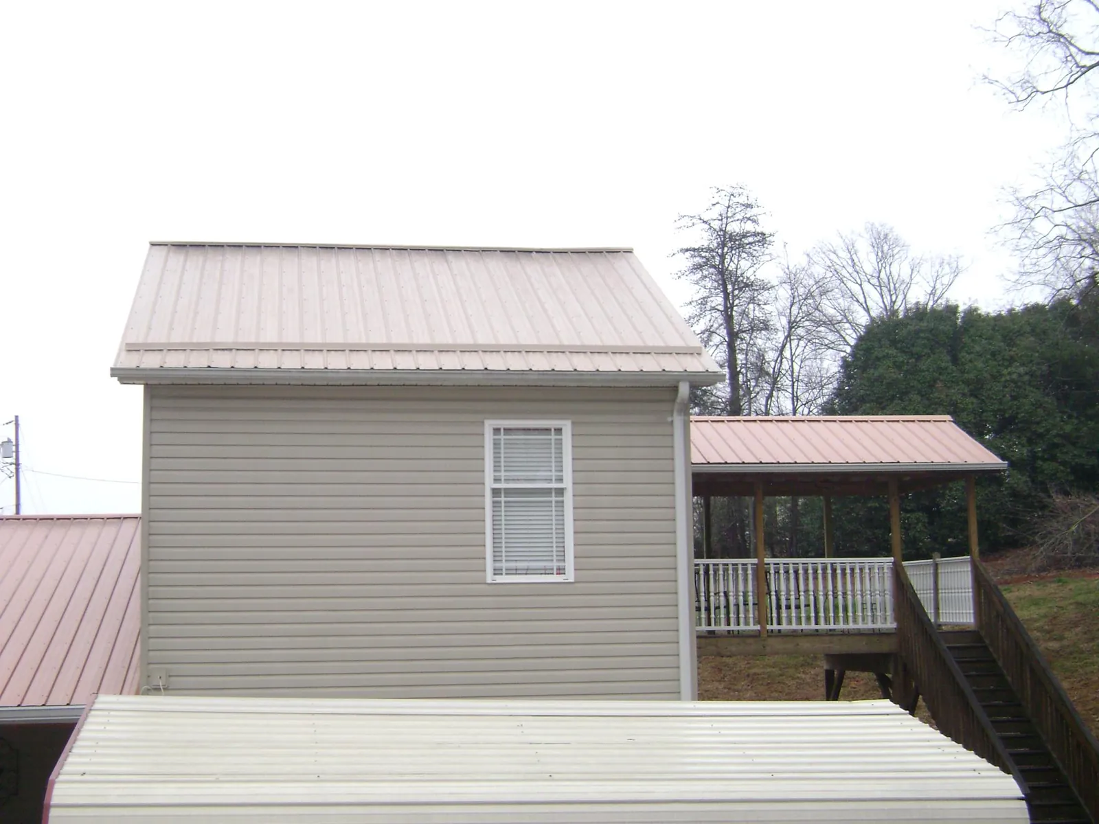 Tan metal roofs on a two story addition and attached porch, from a Roof Replacement job in Bentley